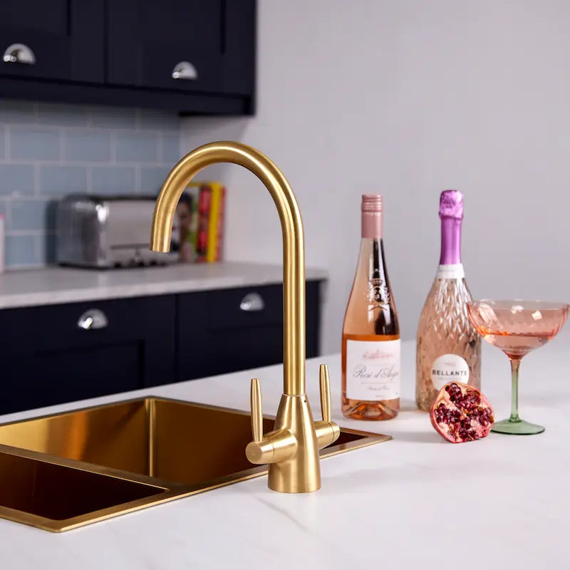 Astrid gold kitchen tap installed on a brushed brass sink in a navy shaker kitchen