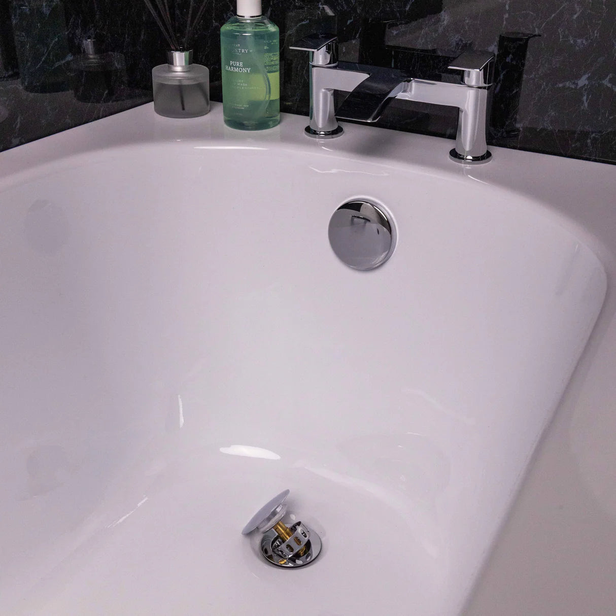 Close-up of a bathtub drain with a stopper, faucet, and toiletries in the background at Irishbath store