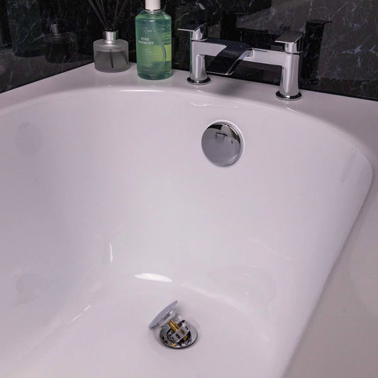 Close-up of a bathtub drain with a stopper, faucet, and toiletries in the background at Irishbath store