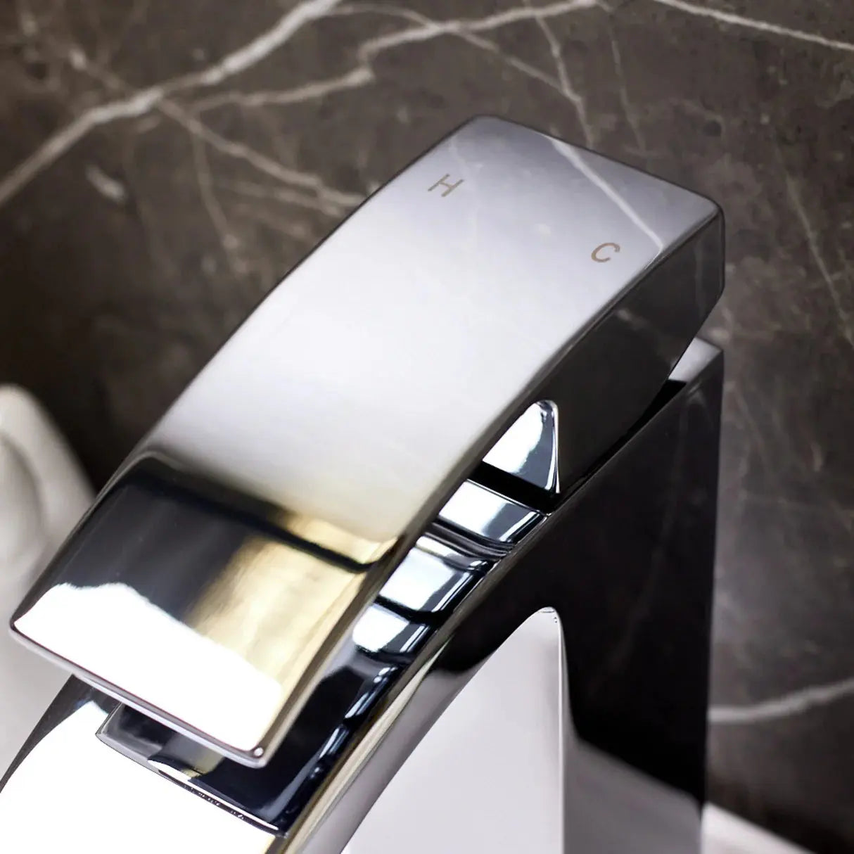 Chrome mixer tap with waterfall spout installed on a white basin with marble wall at Irishbath