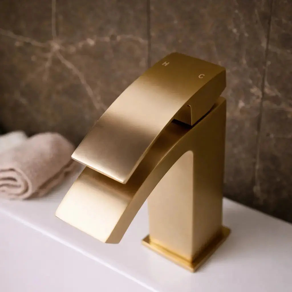 Gold bathroom mixer tap with waterfall spout installed on a white basin with marble wall in Ireland