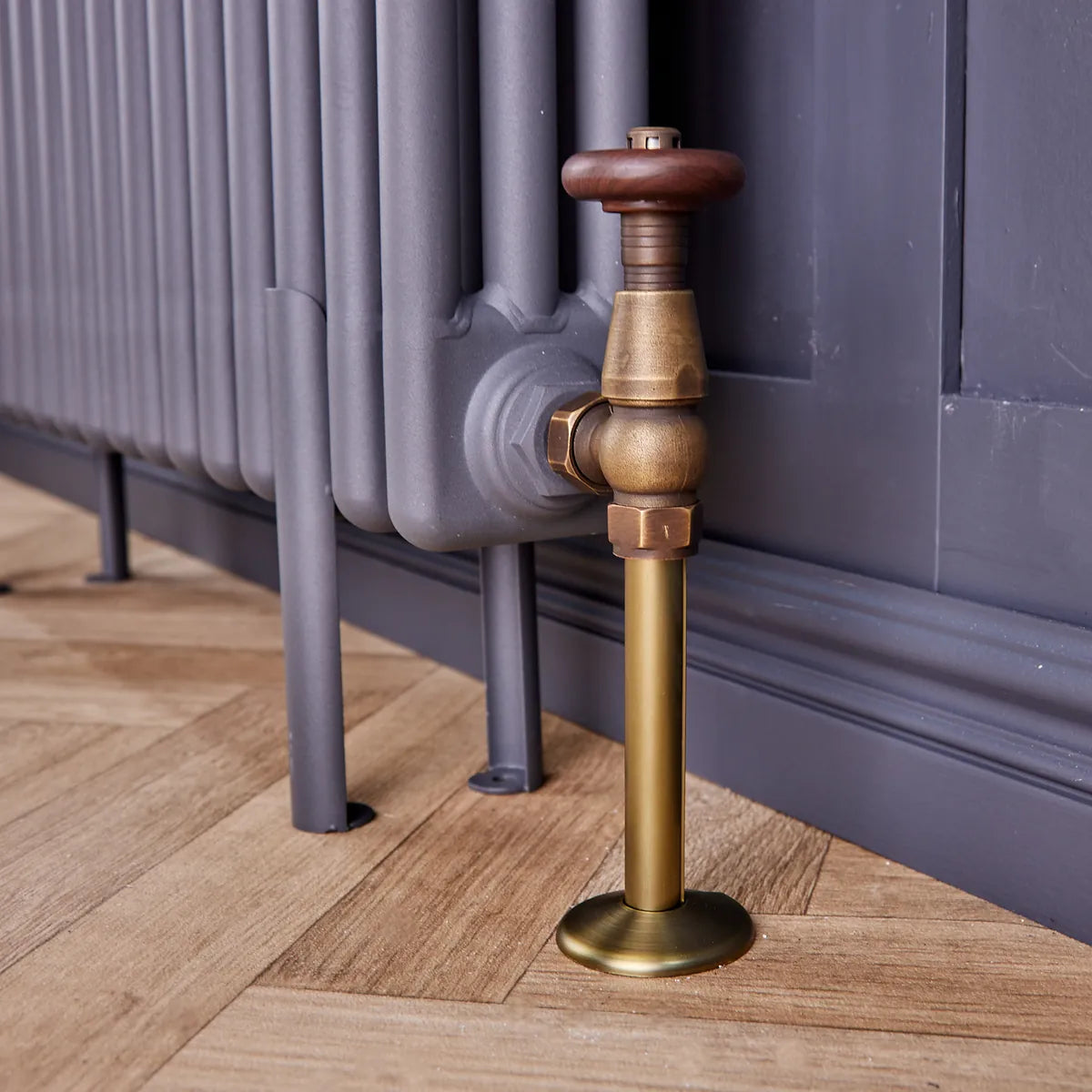 Close-up of an antique brass radiator pipe cover and collar under a traditional valve on a column radiator