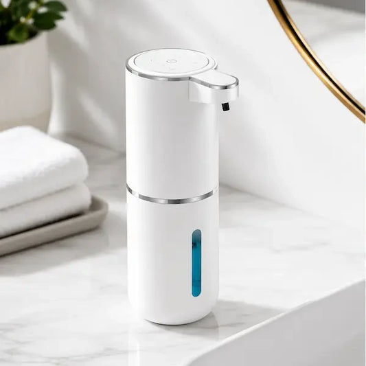 Automatic soap dispenser standing on a marble bathroom basin surround beside folded towels