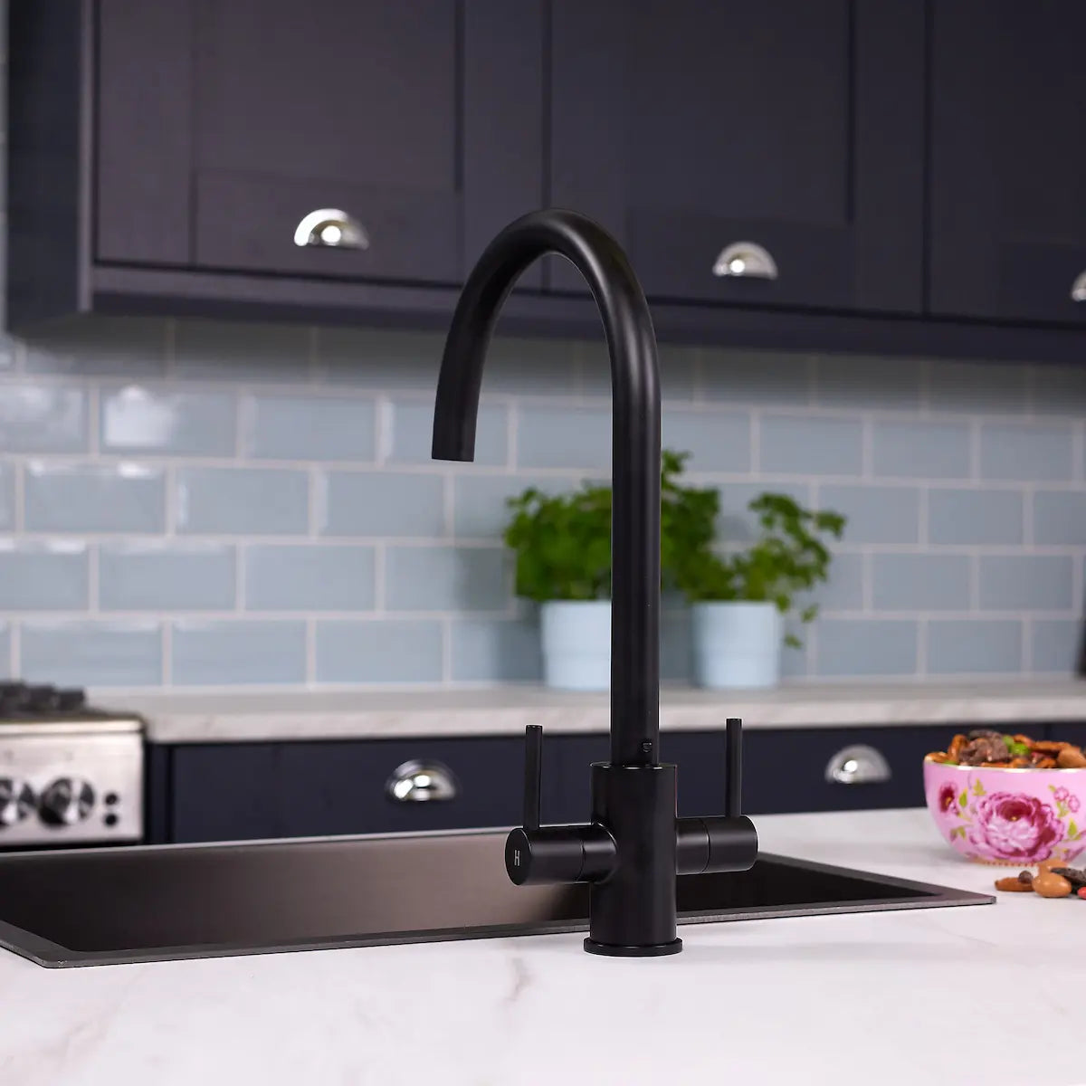 Matt black Adria kitchen tap seen straight on above a black undermount sink, against a blue metro tile splashback