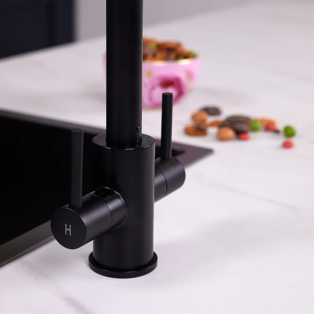 Close view of the matt black Adria tap base and the hot lever, marked H, on a white marble worktop