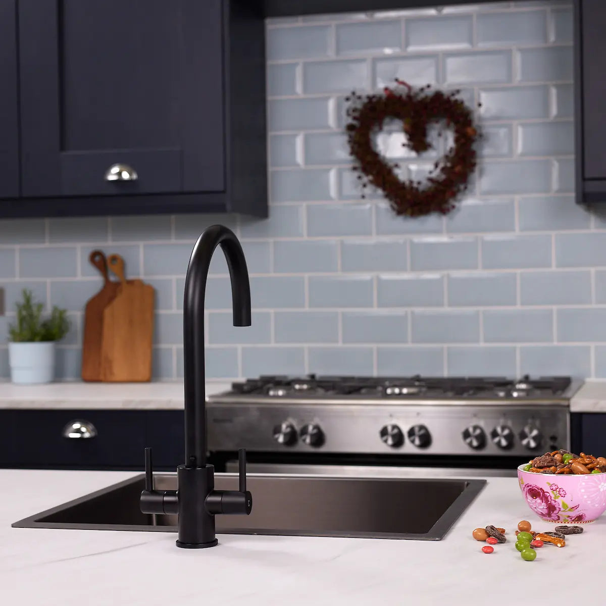 Matt black kitchen tap above a black sink in a navy kitchen with a stainless gas range and blue tiled splashback