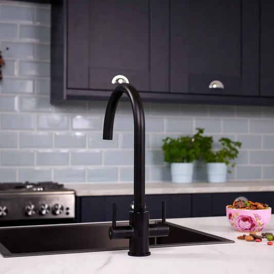 Matt black dual lever kitchen tap fitted to a white marble worktop beside a black sink in a navy shaker kitchen