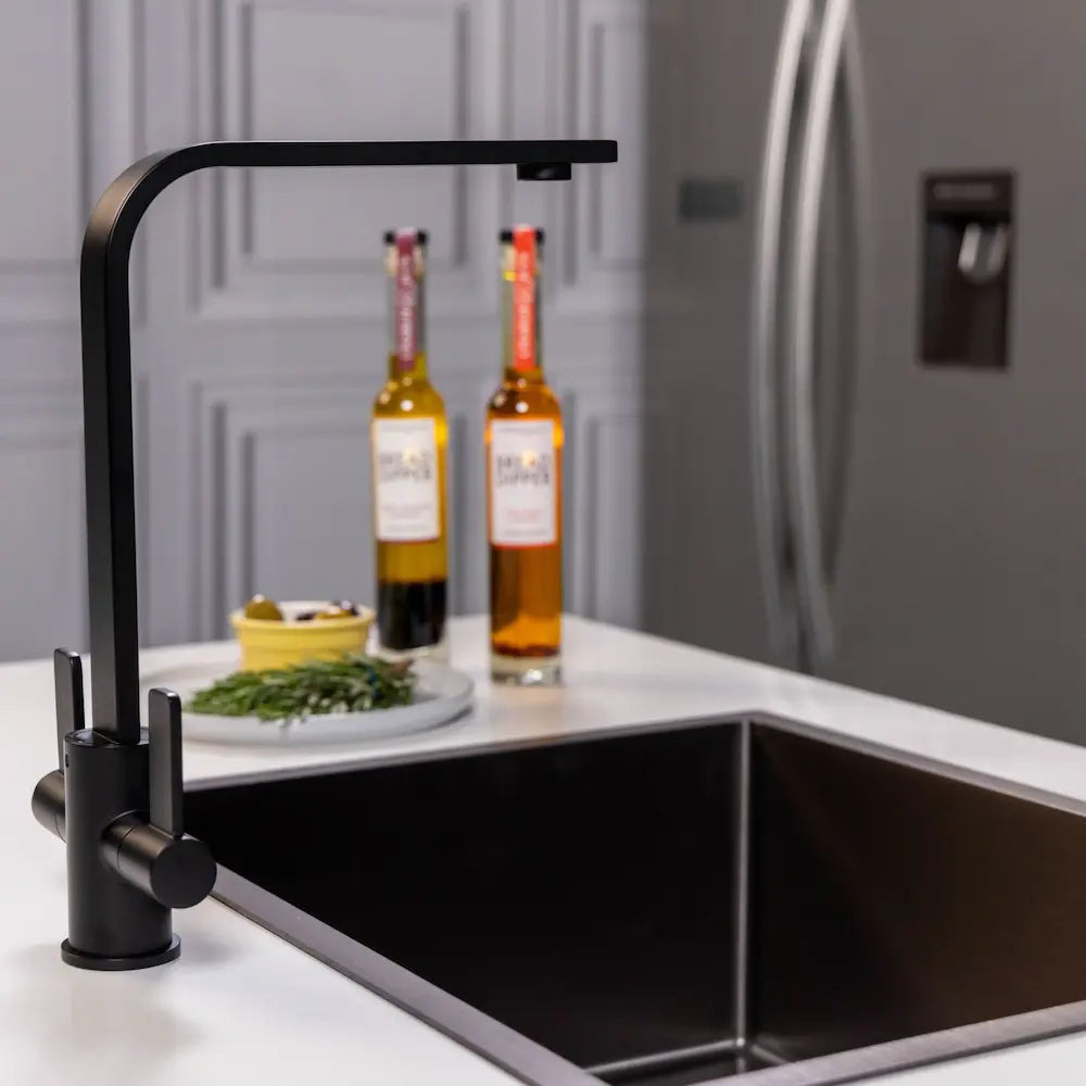 Side view of the matt black kitchen tap beside a black sink in a grey panelled kitchen, with the fridge behind