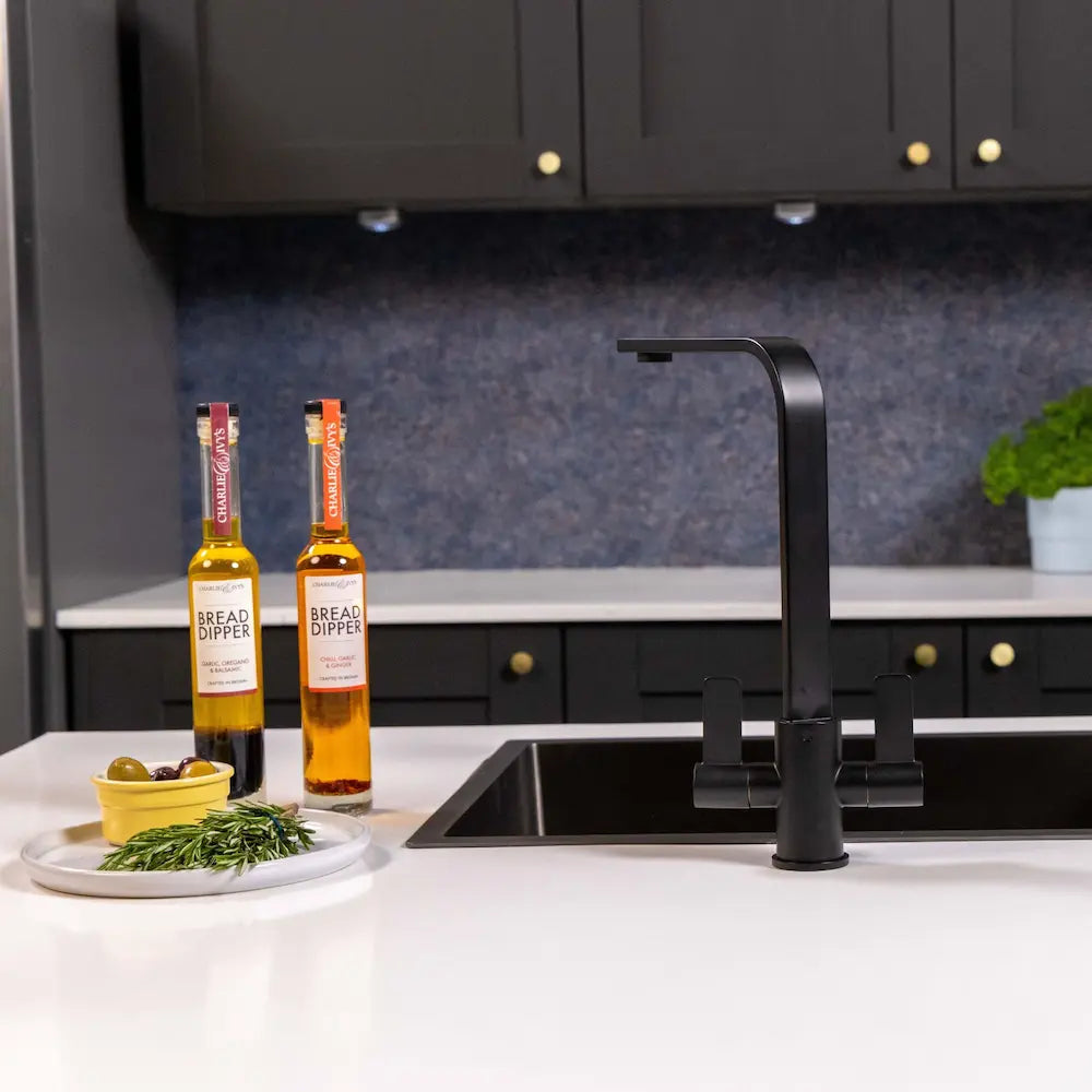 Matt black kitchen tap against a navy splashback with dark cabinets, oil bottles and olives on the worktop