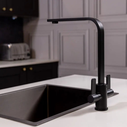 Matt black twin lever kitchen tap fitted to a white worktop beside a black undermount sink in a grey panelled kitchen