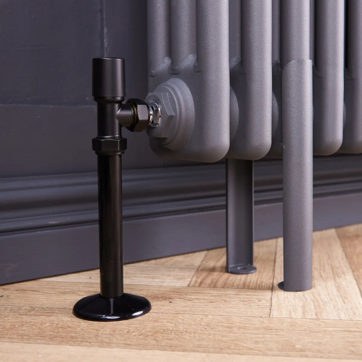 Close-up of a black radiator pipe cover and collar under a black valve on a grey column radiator