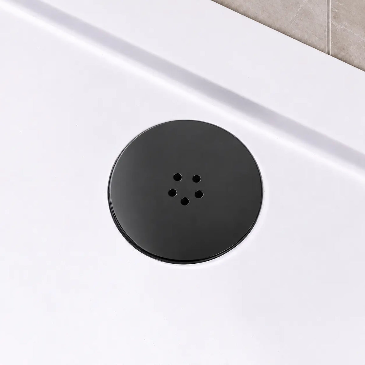 Black shower waste cover fitted in a white shower tray beside a grey tiled wall