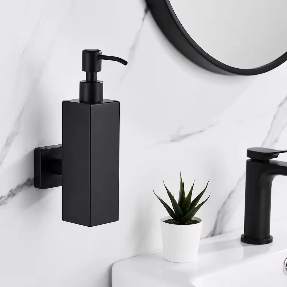 Black soap dispenser mounted on a marble bathroom wall beside a matt black basin tap and round black mirror