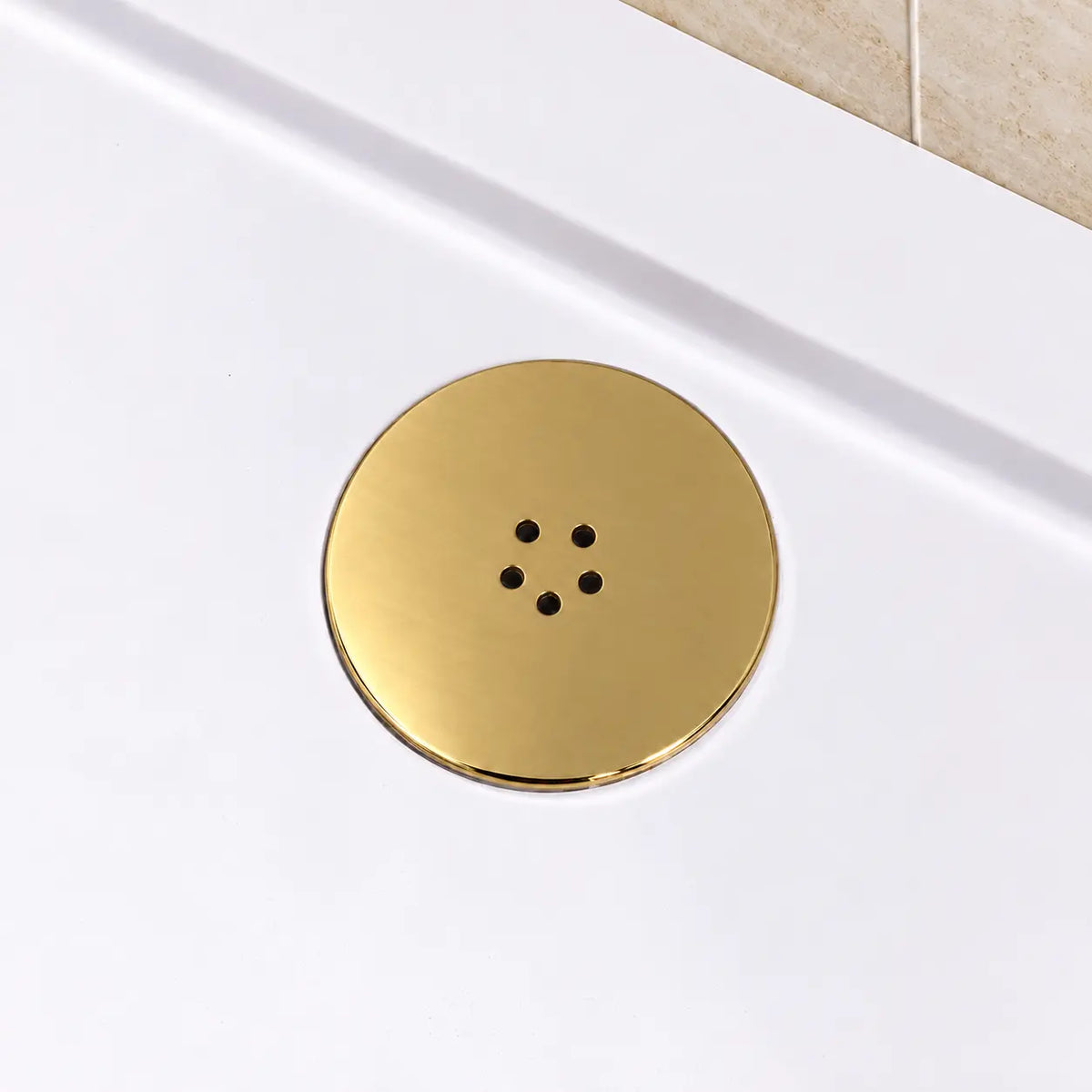 Bright gold brass shower waste cover fitted in a white shower tray beside a beige tiled wall