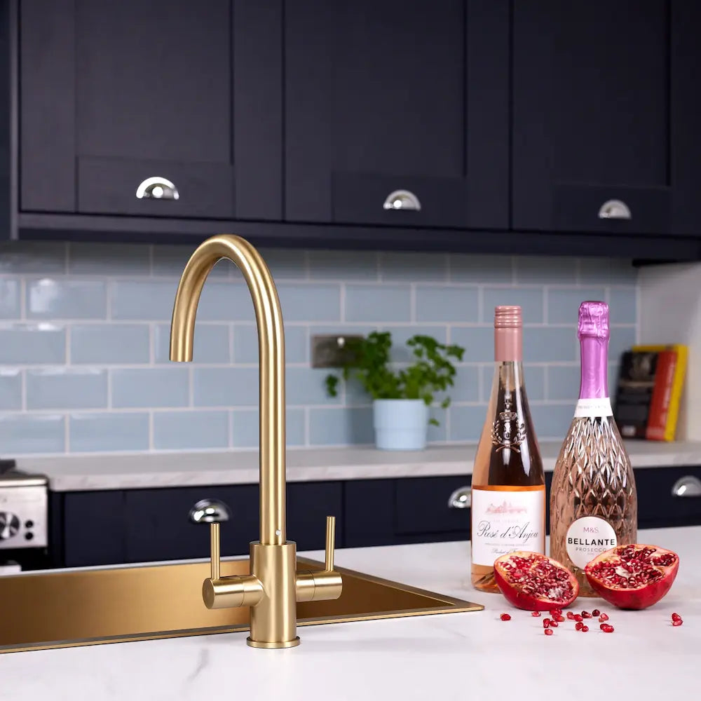 Adria brass kitchen mixer tap fitted beside a brushed brass inset sink on a white marble-effect worktop