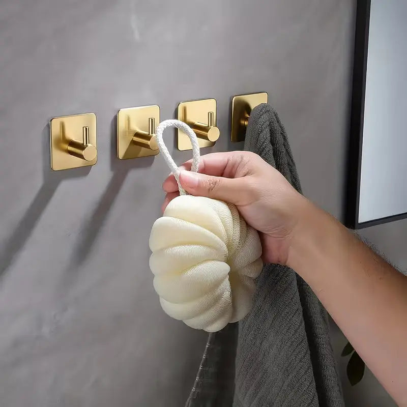 Brushed brass adhesive wall hook holding towel on grey bathroom wall with a man hand