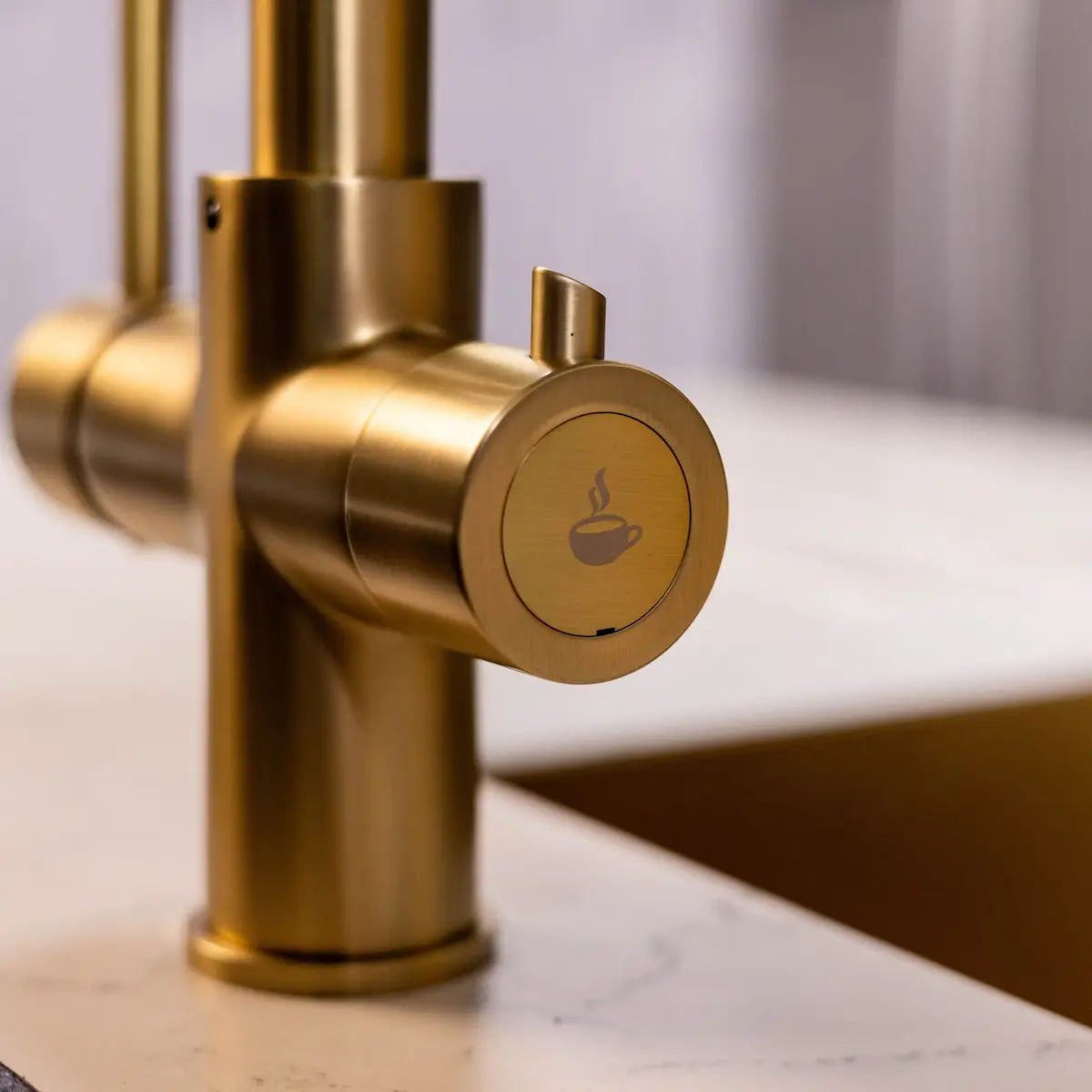 Close view of the boiling water lever on the brushed brass tap, marked with a steaming cup symbol to set it apart from the standard mixer lever