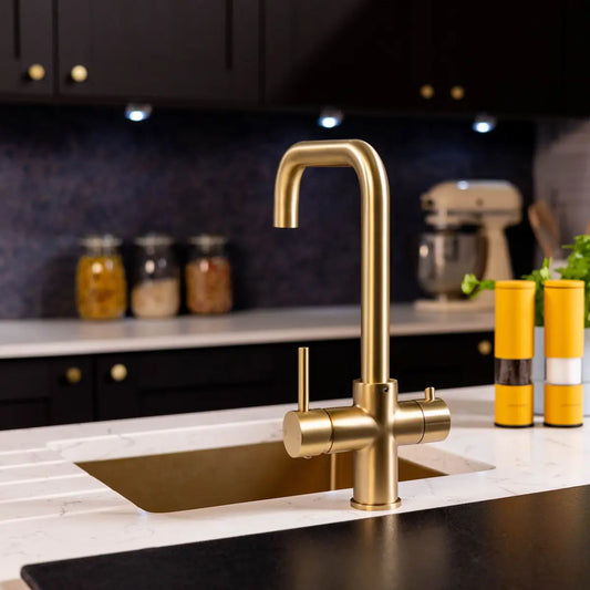 Front view of the brushed brass 3 in 1 boiling tap fitted over a brass undermount sink, showing the squared spout and both levers