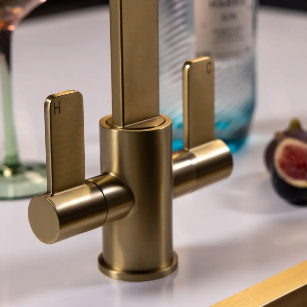 Close view of the two quarter-turn levers and the brushed brass body, with the hot lever marked H