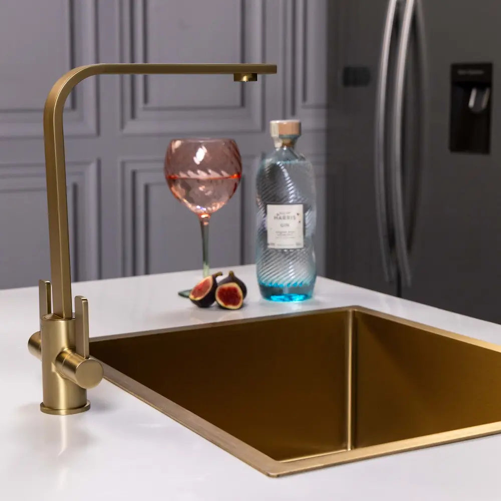 Brushed brass kitchen tap by Ellsi (etal) and gold sink in a grey panelled kitchen, with the fridge visible behind
