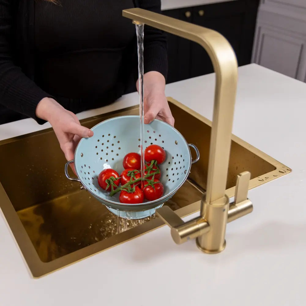 Someone rinsing tomatoes in a colander under the running brushed brass kitchen tap