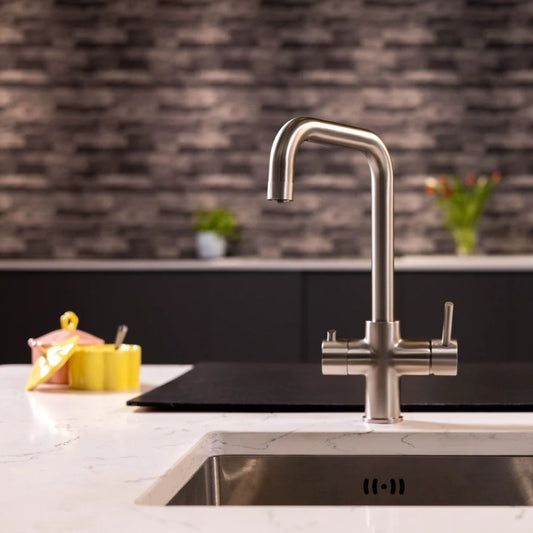 Brushed steel boiling water kitchen tap with a squared swivel spout over an undermount sink on a white marble-effect worktop