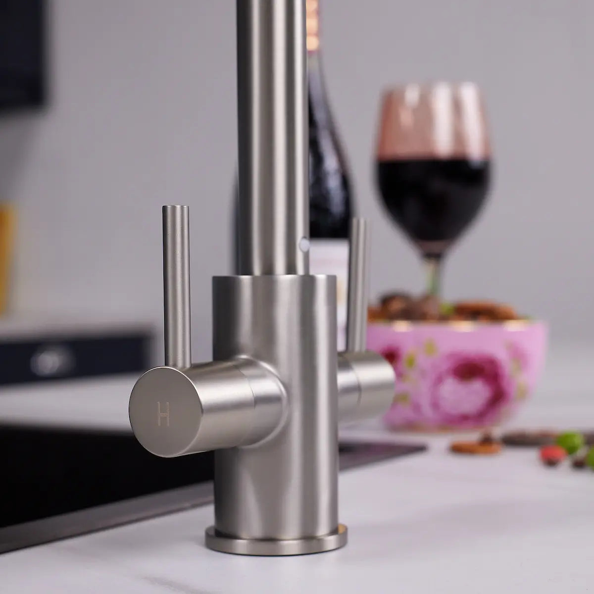 Close view of the brushed steel Adria tap base and the hot lever, marked H, showing the fine brushed grain