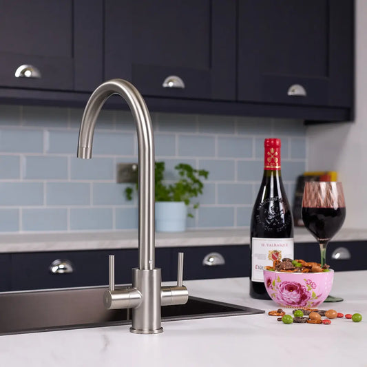 Brushed steel dual lever kitchen tap fitted beside a stainless steel sink in a navy shaker kitchen with blue metro tiles