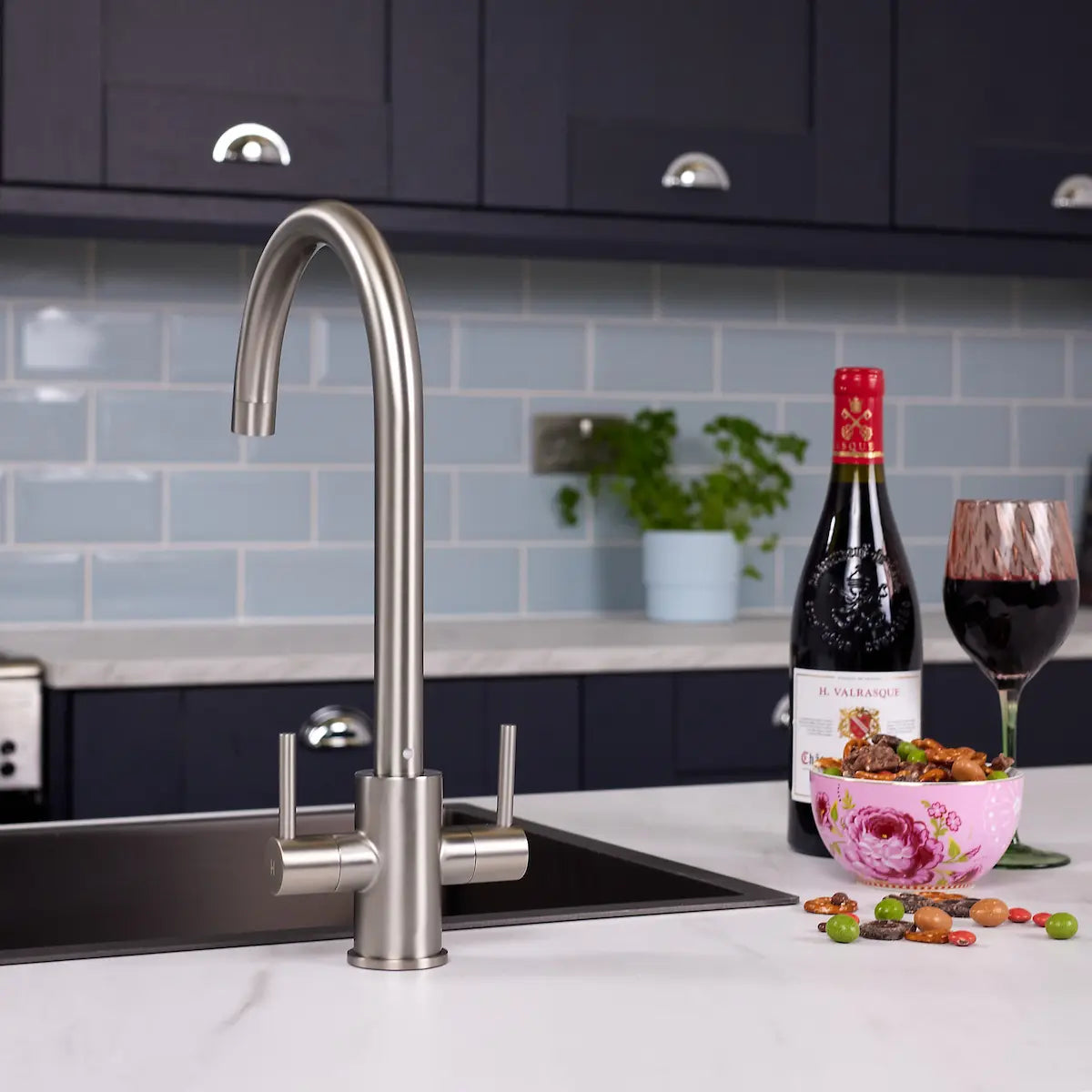 Brushed steel Adria kitchen tap on a white marble worktop above a stainless steel sink, with navy cabinets behind