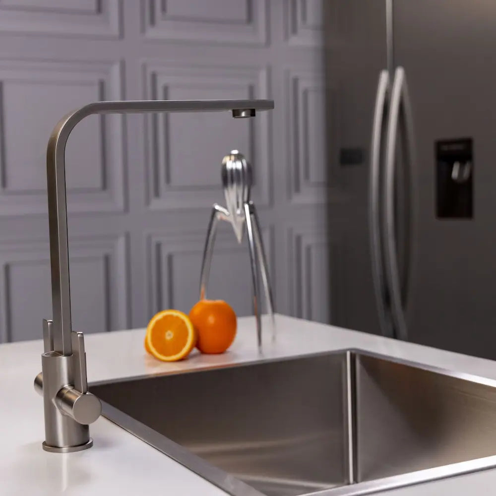 Brushed steel kitchen tap over a stainless sink in a grey panelled kitchen, with a stainless fridge behind