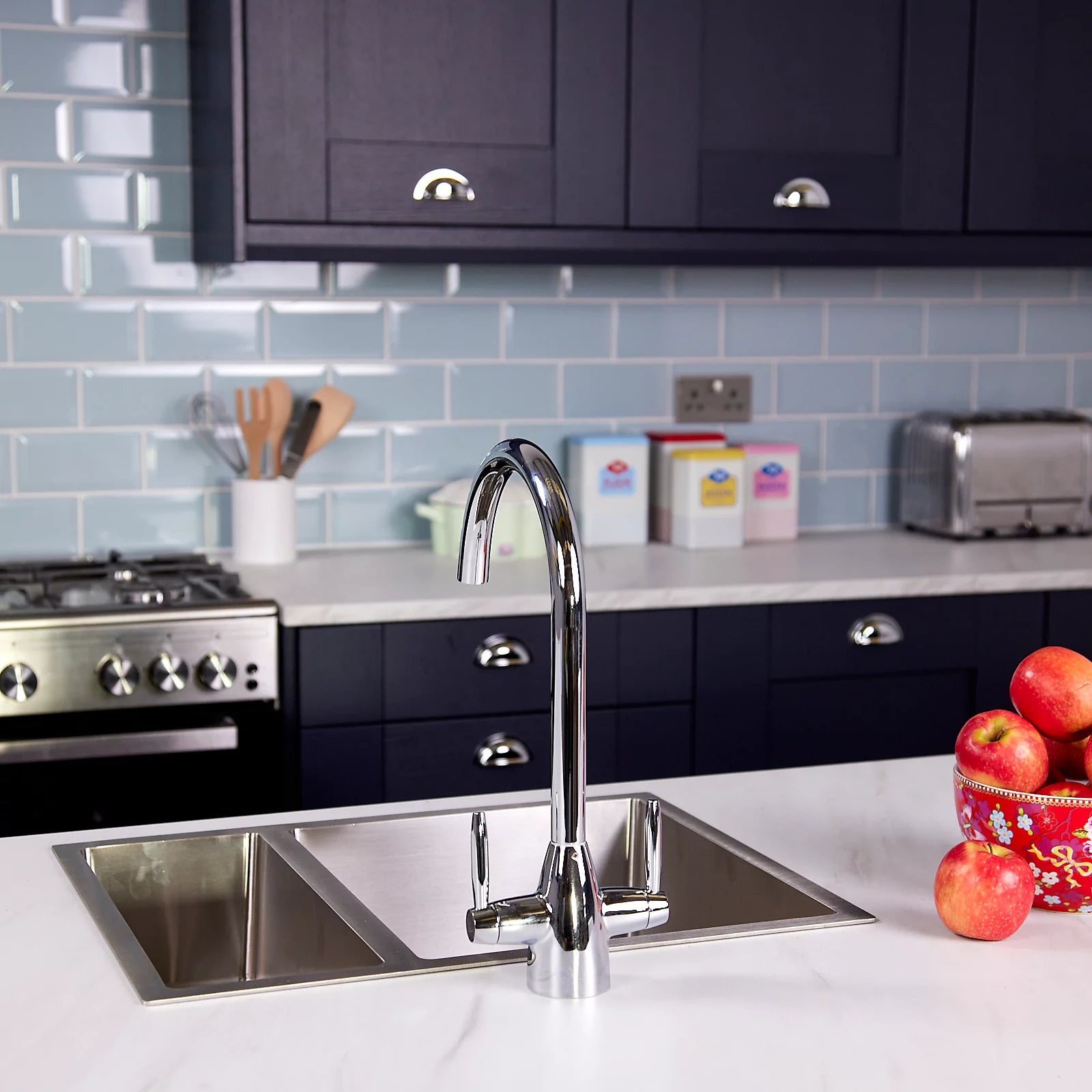 Chrome dual lever kitchen tap seen from the right, against navy shaker cabinets and a white marble worktop