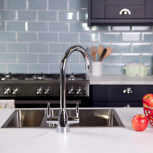 Chrome dual lever kitchen tap fitted to a stainless steel sink in a navy kitchen, with pale blue metro tiles and a range cooker behind