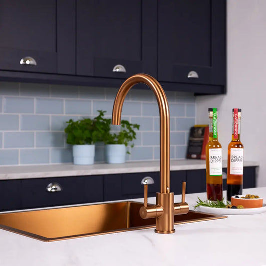 Brushed copper dual lever kitchen tap over a copper inset sink, with navy shaker units and blue metro tiles