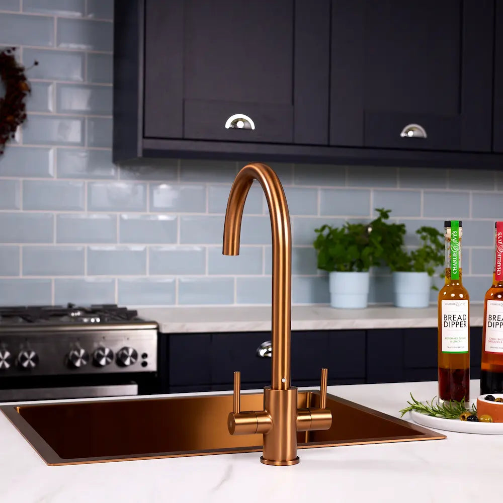 Copper kitchen tap with twin levers on a white worktop in a navy kitchen with a range cooker