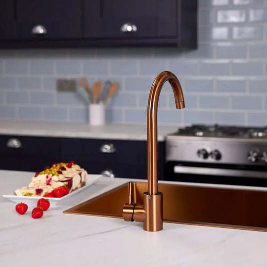Brushed copper single lever kitchen tap over a copper inset sink, with navy shaker units and a range cooker behind