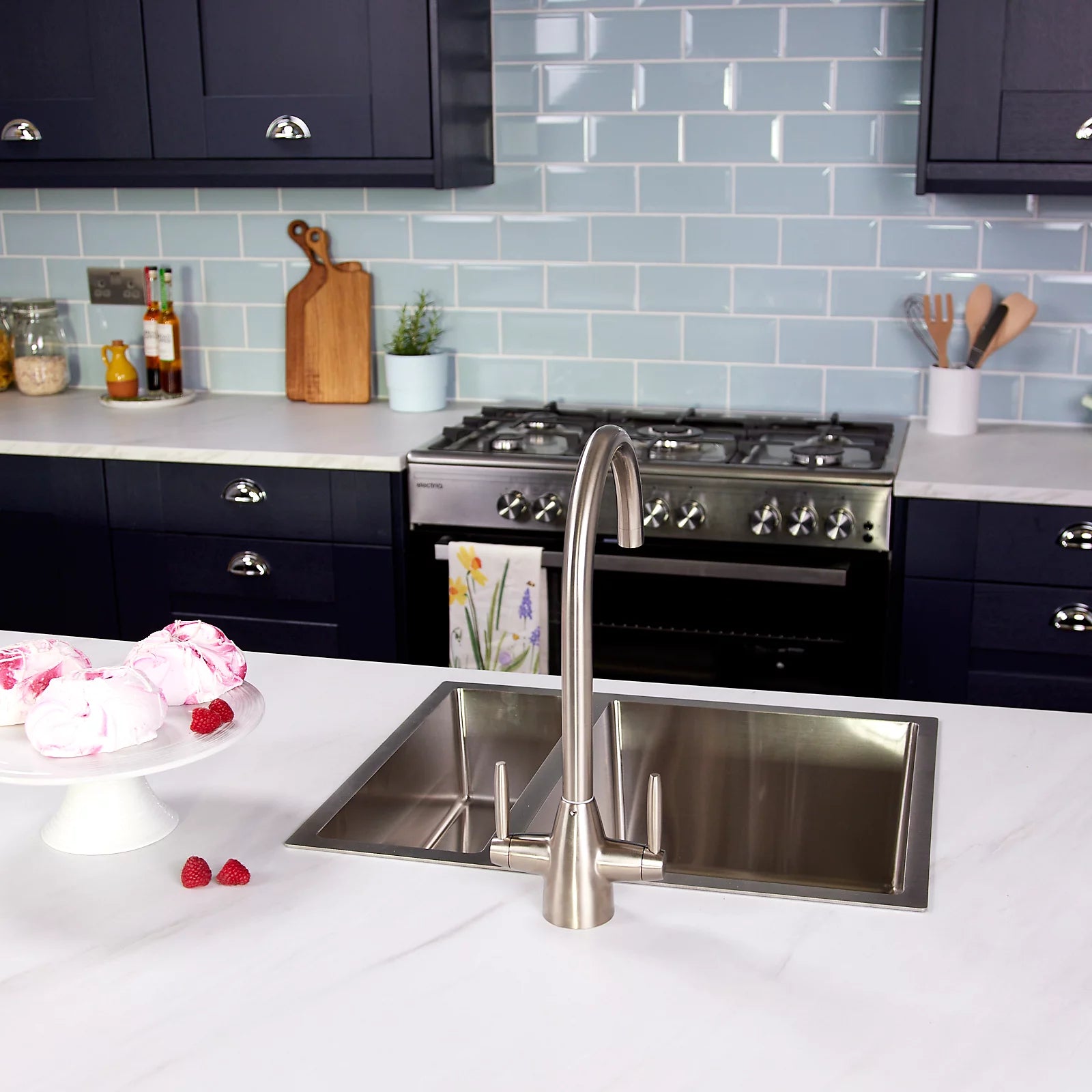 Pewter Astrid kitchen tap in a navy kitchen, seen past a cake stand with the range cooker and open shelving behind