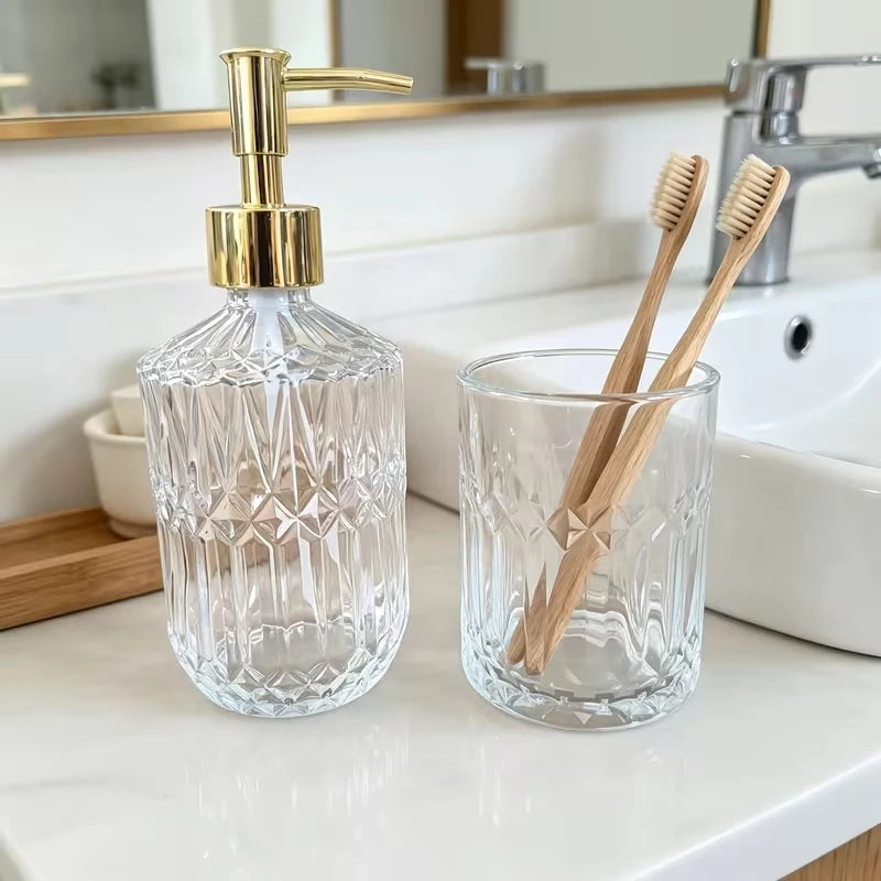 Cut glass soap dispenser and toothbrush holder standing on a marble basin surround, gold plated pump