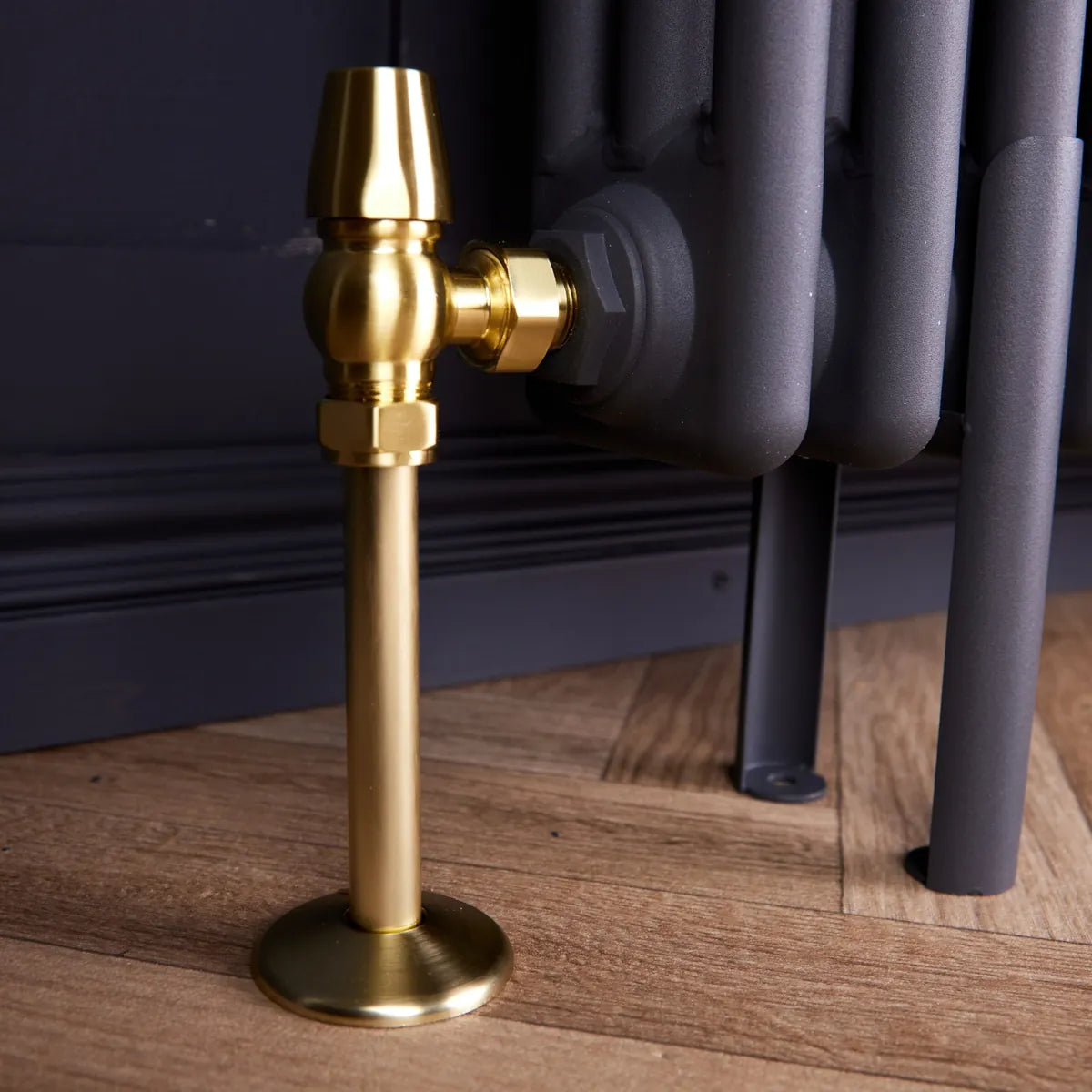 Close-up of a brushed brass radiator pipe cover and collar under a brass valve on a grey column radiator