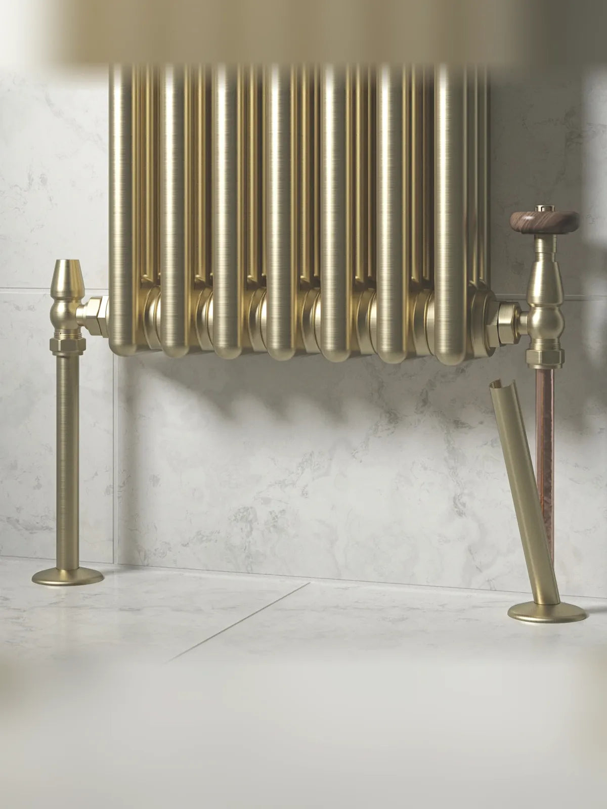 Brushed brass radiator pipe covers fitted to a brass column radiator with traditional valves, one sleeve shown mid-fit