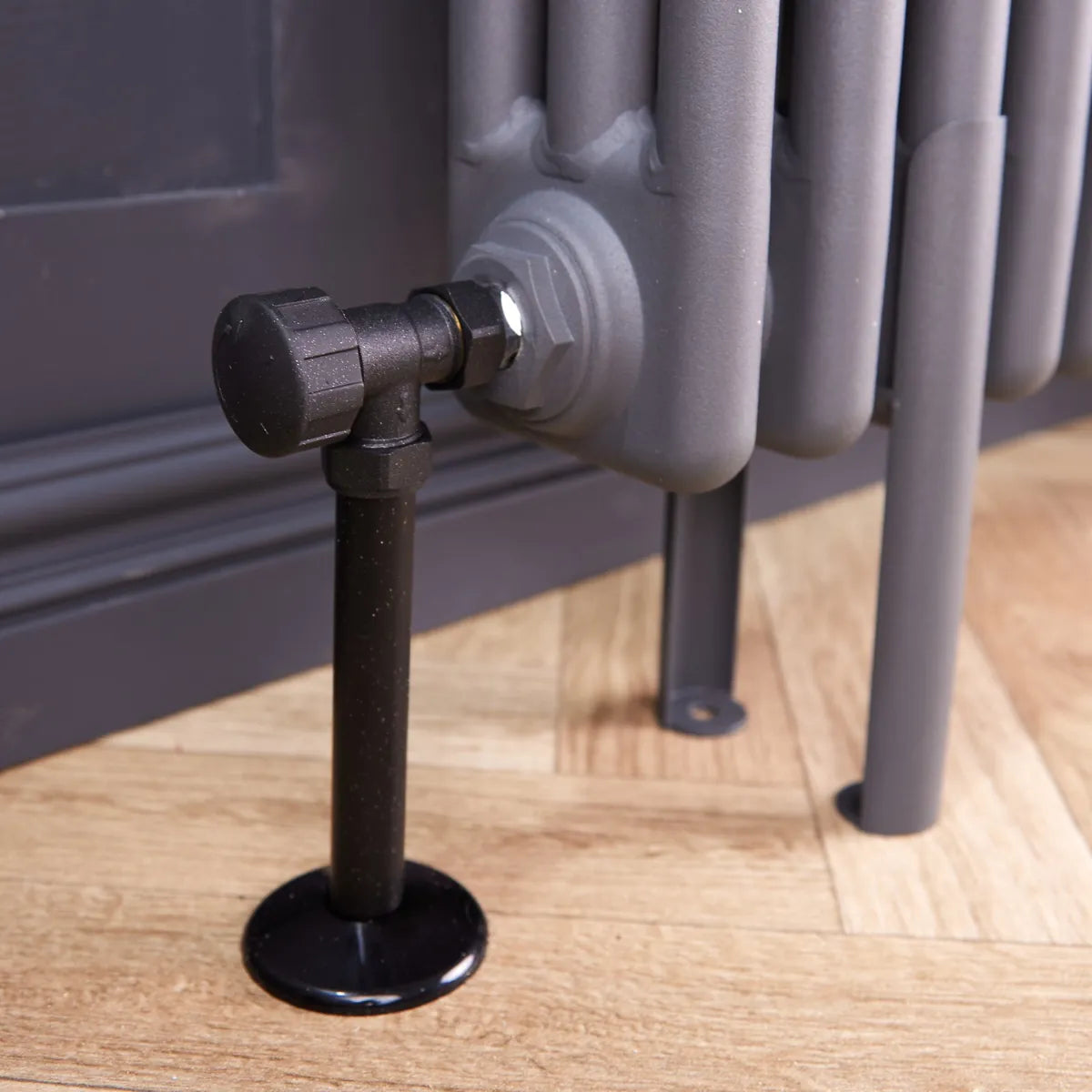 Close-up of an anthracite grey radiator pipe cover and collar under a dark valve on a grey column radiator