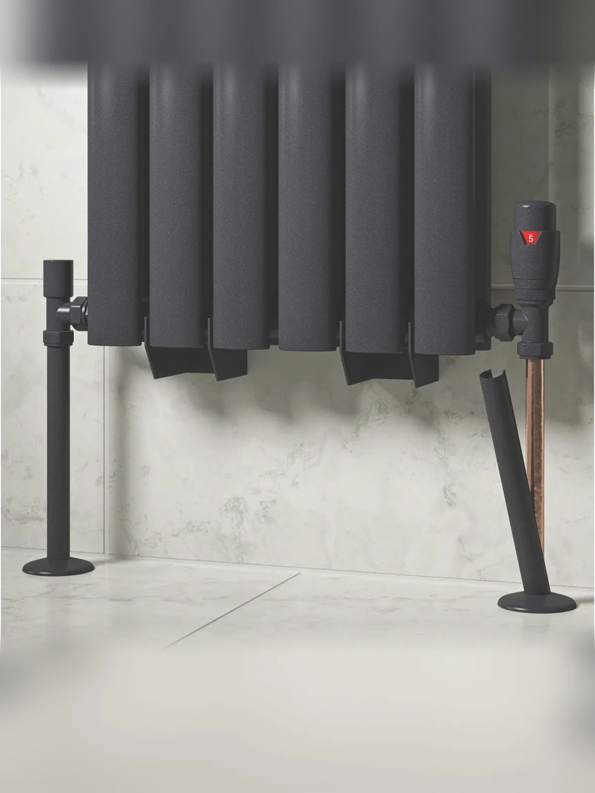 Anthracite grey radiator pipe covers fitted to the pipes of a dark radiator, one sleeve shown mid-fit beside the valve