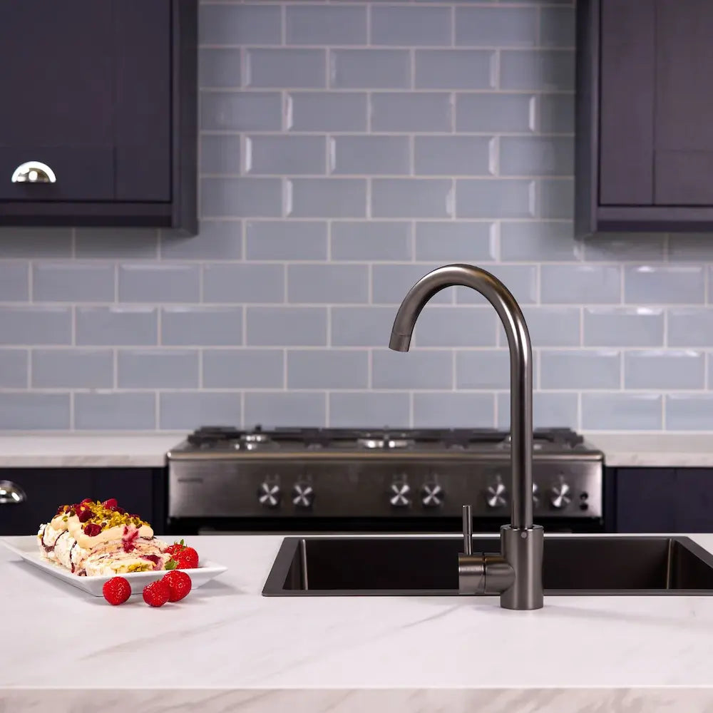 Gunmetal single lever kitchen mixer tap over a black sink, with a range cooker, navy shaker units and blue metro tiles behind
