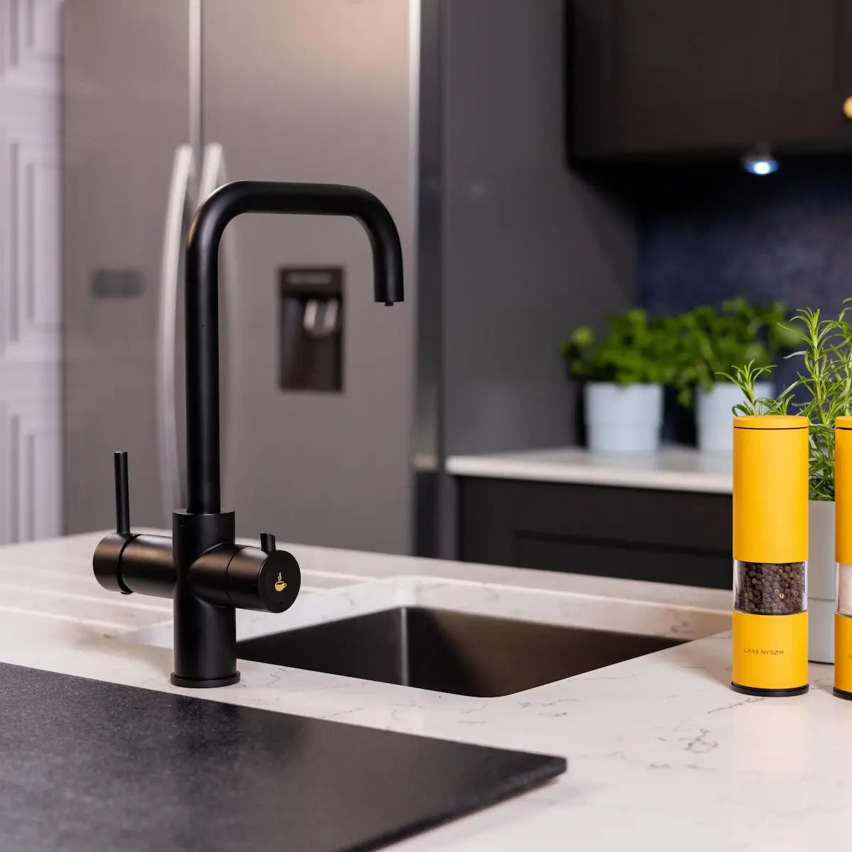 Matt black boiling water tap seen at an angle beside a black sink, showing the squared spout and both levers