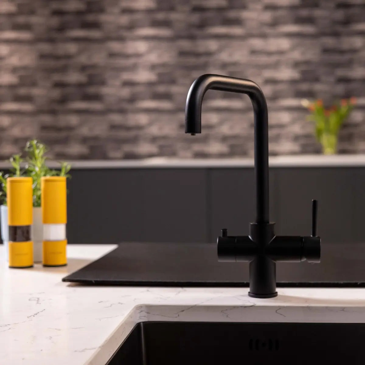 Front view of the matt black 3 in 1 hot water tap fitted beside a black undermount sink in a dark kitchen