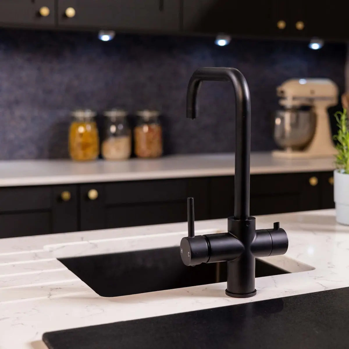 Matt black instant hot water tap on a marble worktop, with a navy splashback and a stand mixer on the counter behind
