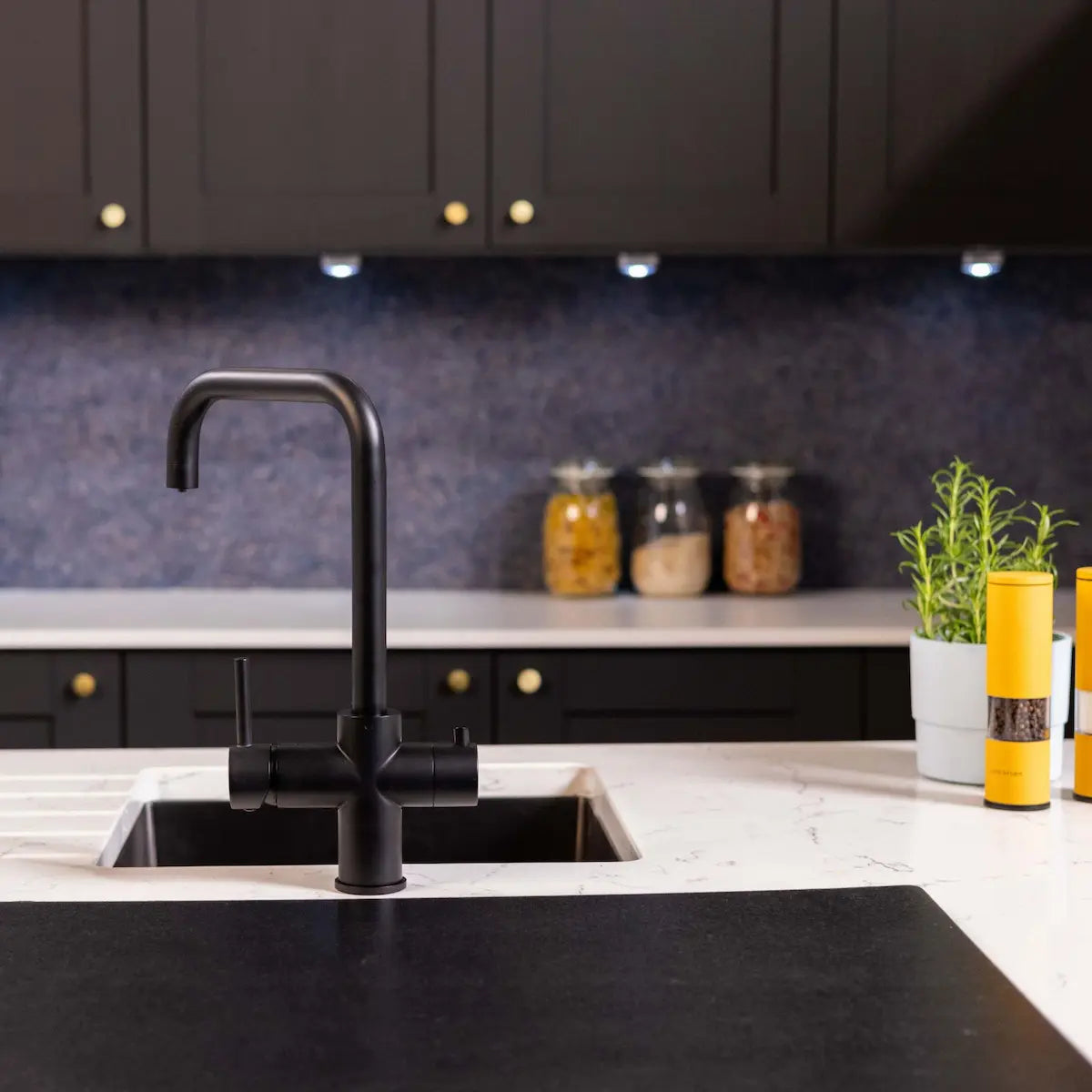 Matt black 3 in 1 boiling water tap in a dark kitchen with a navy splashback, black cabinets and storage jars on the counter