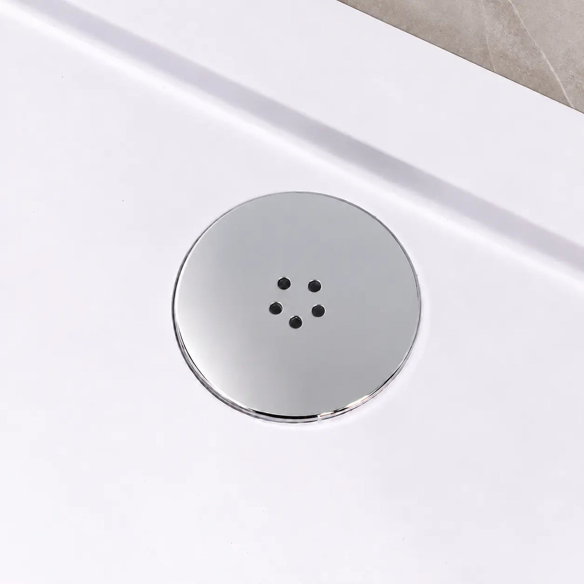 Polished chrome shower waste cover fitted in a white shower tray beside a greige tiled wall